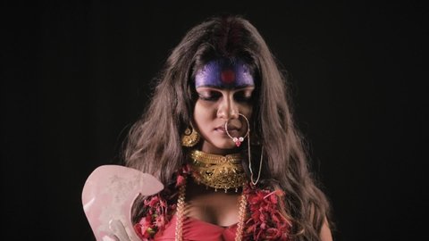 Live Indian Goddess Kali opens her eyes and looks at camera, Indian goddess cosplay with long hair and dark background in studio