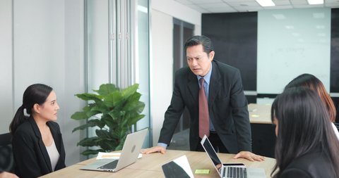 Angry asian boss yelling at colleagues during a meeting with his team in a meeting room.