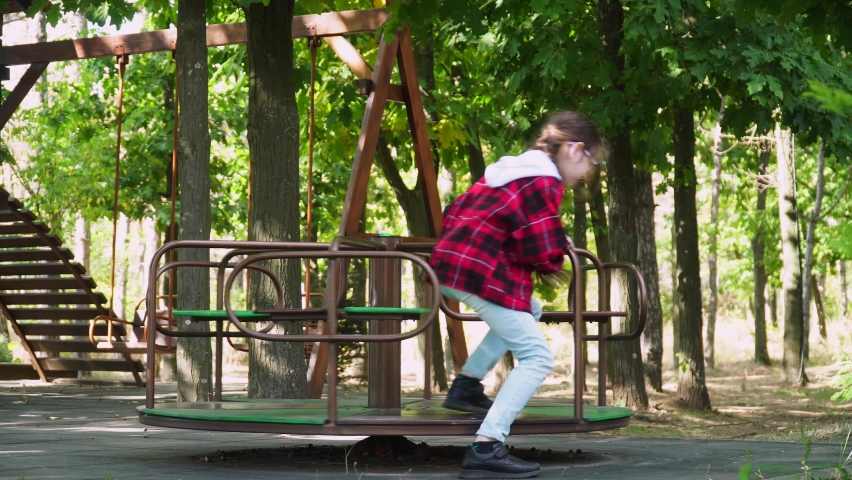 girl rides on swing waving her hand. Cute baby girl enjoying swing in the park