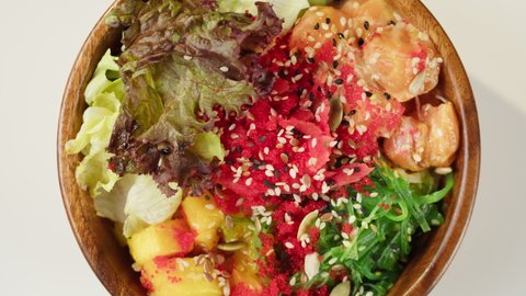 Poke bowl salad on white background. Sliced vegetables, red fish and sesame seeds. Traditional Hawaiian cuisine close-up. Healthy vegetarian food. Asian vegan raw meal rotating.