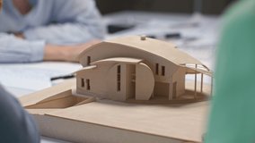 Architects and designers working on house layout in modern office. Group of creative people at table talking on wood maquette and discussing layout design. Specialists look at projection of home model - Powered by Shutterstock - Get 15% off with code: PIKWIZARD15
