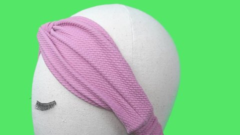 A mannequin wearing dusty pink color handmade headband made out of jersey fabric with greenscreen background. A hairband or headpiece with twist pattern in front.