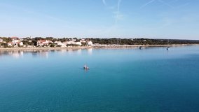 Aerial view video of active family on SUP stand up paddle vacation. Parents and children enjoying summer vacation on paradise Mediterranean beach in Adriatic Sea, Silba, Croatia.