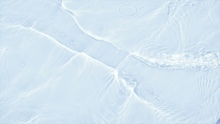 Crystal water in the pool on a sunny day in slow motion.  Beautiful transparent clear calm water surface texture with splashes and waves in slow motion. Trendy abstract nature background in 4K