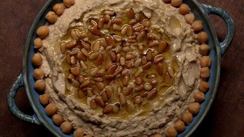 Homemade hummus spread with olive oil and pine nuts. Top view. Table rotate. ProRes