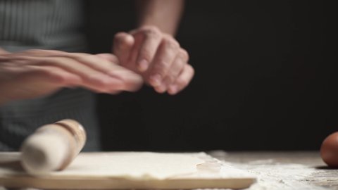 A baker prepares yeast dough by rolling it out with a rolling pin in a rustic style on a dark background