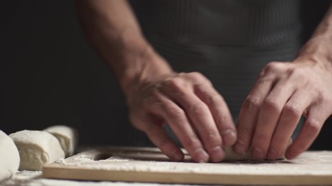 A baker prepares yeast dough by rolling it out with a rolling pin in a rustic style on a dark background