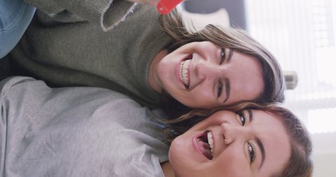 Vertical shot of a Caucasian lesbian couple having a video call, smiling at the camera and holding keys. Domestic life concept.