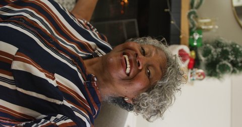 Vertical shot of a senior African American woman having a video call, with a fireplace and Christmas decorations in the background. Seniors, technology, and Christmas concept.