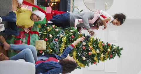 Vertical shot of an African American family decorating a Christmas tree, man being handed a star-shaped tree topper by his wife, a girl sitting on his shoulders. Family and Christmas concept.