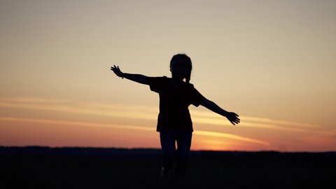 Little girl runs on the green grass. Happy child in a nature park at sunset. A cheerful girl runs in the field. Happy cute child in nature. Sunset in the summer. Girl running on the grass at sunset