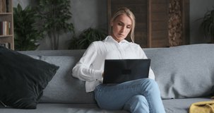 Thoughtful young woman freelancer typing on laptop sitting sofa. Relaxed female writing article, chatting, browsing social media, distance internet job concept.