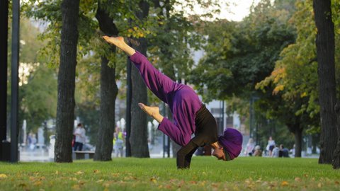 Strong active muslim girl in hijab woman yogi sportswoman doing yoga workout in park on green lawn doing balance handstand training holding leg in air acrobatic element moves actively stretching asana