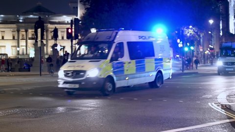 LONDON - NOVEMBER 5, 2021: Police vans with blue flashing lights speed through traffic at Trafalgar Square at night