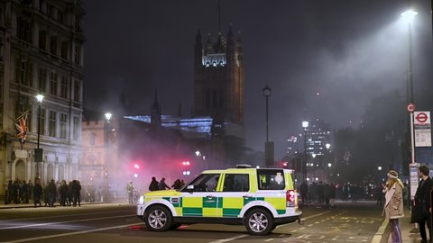 LONDON - NOVEMBER 5, 2021: Paramedic in 4x4 waits near Parliament Square with smoke, protesters and Houses of Parliament in background