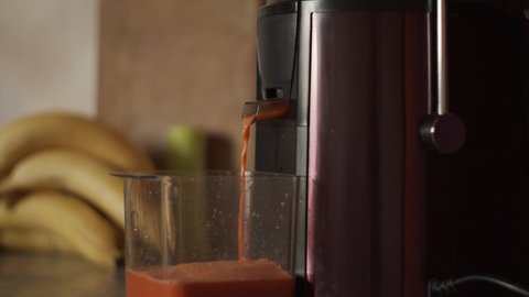 4K Centrifugal juicer pressing homemade carrot juice. Filing plastic cup with juice. Making freshly squeezed fruit and vegetable juice, close-up. Kitchen electrical appliances. Healthy drink, bananas,