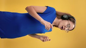 VERTICAL VIDEO POV happy woman singing song dancing enjoying freedom isolated on orange background. Smiling pleasant female wearing headphones listening music audio sound with positive emotion