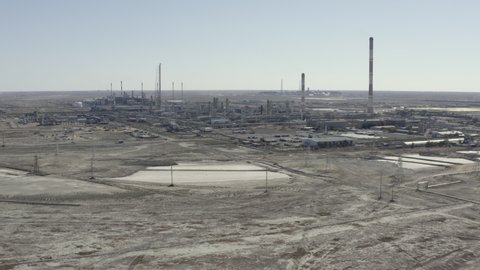 A huge oil refinery with tall pipes stands in a sandy desert. Aerial footage of an oil and gas plant in the endless desert steppe. Large oil production.