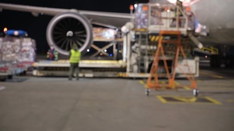 Blurred footage of aircraft ground handling in the International airport terminal. Baggage and Freight Handling on the inbound aircraft. Ramp service at night.  Video with defocused effect. 