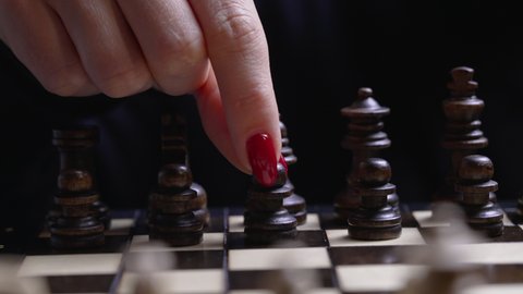 Woman player playing board intelligence game - wooden chess. Close- up view of female arm with red nails moves a chess piece pawn, first move. Sport, success strategy concept.