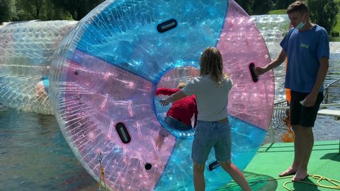 Munich, Bavaria, Germany- July 25, 2021: Olympic park . Entertainment for children, amusement park rides. Floating plastic water walking barrels. Kids zorbing. 4K