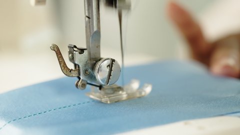 Close up of female hand working with sewing machine showing process of textile making garment.	