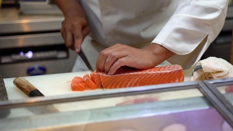 A master chef is using very sharp knife to cutting or slicing a big piece of salmon meat on the cutting board. Expertise cooking action 4k footage, Close-up and selective focus.