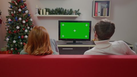 Family couple watching a green screen TV model sitting on the couch in the living room during the Christmas season. TV shows or news in your home or Christmas commercial.