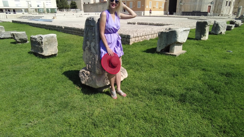 Elegant lady with hat in the Ancient Roman square of Zadar of Croatia, capital of Dalmatia. Old Roman Forum with Cathedral of St. Anastasia and Church of St Donatus with the bell tower.