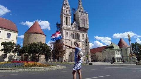 Happy woman with Croatian flag in the square of Zagreb Cathedral of Zagreb city, capital of Croatia in Europe. Colonnade monument of the Assumption of the Blessed Virgin Mary.