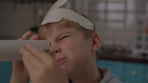 Kid eating sweets while playing pirate's game with paper telescope and headwear with skull and crossbones. Preschool boy in pirate's hat smiling at camera.