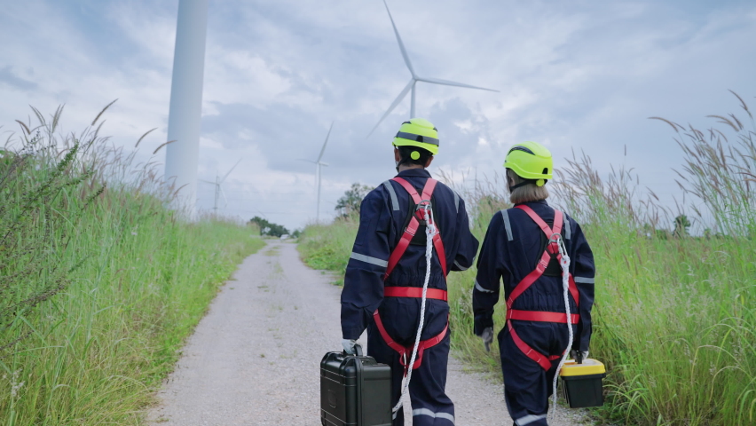 Two maintenance engineers in safety gear working at height walking to the wind turbine to check the operation of the wind turbine, clean energy concept, renewable energy, save the world. Royalty-Free Stock Footage #1082192801