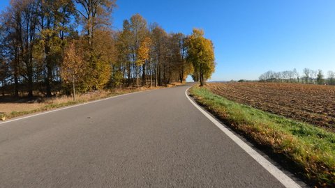 Car drive in fall autumn landscape, POV view from car, fall colored trees in countryside landscape with blue sky in sunny day.