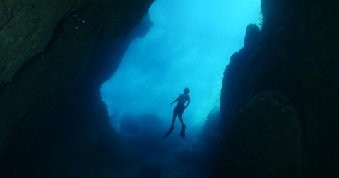 free diver in acave underwater going out of the cave in blue light ocean topography and human scenery of sports