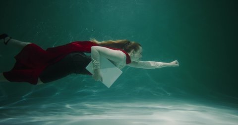 CUSTOMER SERVICE. Beautiful young business woman with red superhero cape suit swims underwater with laptop slow motion.
