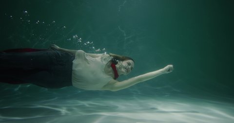 Superwoman concept. Cinematic slow motion, beautiful young business woman with red cape swims underwater slow motion.