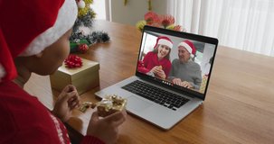 African american woman with santa hat using laptop for christmas video call with family on screen. christmas, festivity and communication technology.