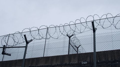 High tensile chain-link fence with electric barbed wire of the prison  with a grey cloudy sky background