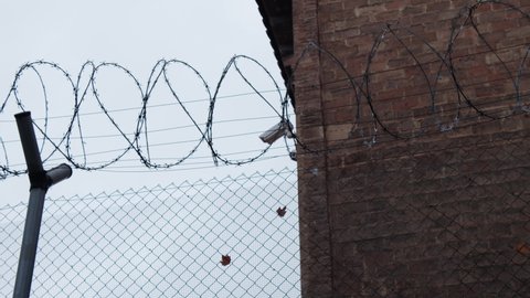 Outdoor surveillance camera controlling the perimeter of the prison yard over the tall barbed-wire fence.