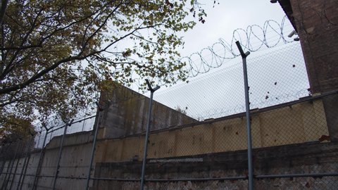 The long barbed-wire fence around the prison yard controlled by an outdoor surveillance camera.