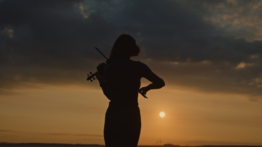 Silhouette of woman from the back with short haircut playing violin outside, in counter sunrise light, getting inspiration of beautiful nature, Slow motion.  Royalty-Free Stock Footage #1082208425