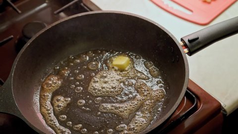 Close-up view of woman adding fresh vegetables from cutting board to frying pan with melted butter for frying, slow-motion slowed down four times