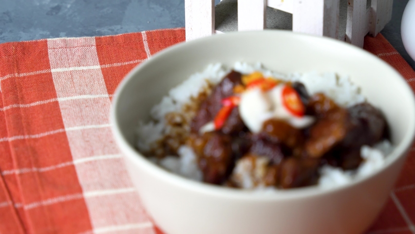 a rice bowl of chinese braised beef shank topped with red onion and chili pepper