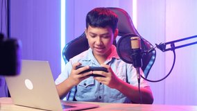 Excited Asian Kid Boy Playing Video Game With Mobile Phone Then Smiles To Camera While Live Stream
