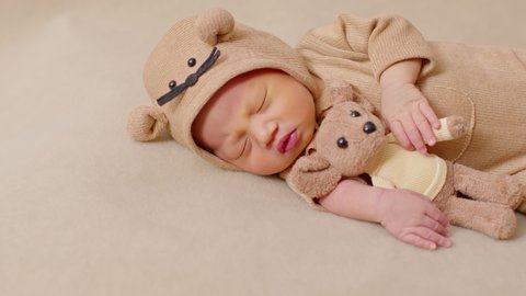 happy newborn baby weaing cute Mouse costume lying sleeps and hug doll on Beige background comfortable and safety.Cute Asian infant sleeping and napping on baby bed.Newborn Baby photography concept