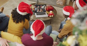 Diverse family with santa hats using laptop for christmas video call with happy family on screen. christmas, festivity and communication technology.