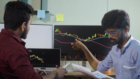 Traders analyzing by discussing about stock market charts while working at office - concept of teamwork, learning or planning share market strategy and financial investment.