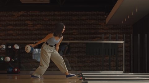 Alone Caucasian brunette woman throws a bowling ball and knocks out a shoot with one throw dances rejoices and jumps with happiness