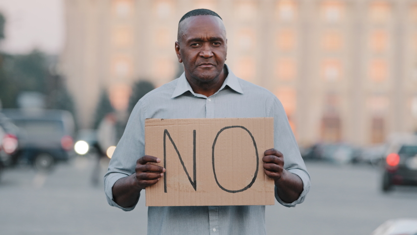 Black immigrant person holding cardboard slogan banner with text no, African American man standing in city disagree refusal against vaccination. Stop racism discrimination political protests concept Royalty-Free Stock Footage #1082232170