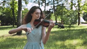 A young girl plays the violin in a city park. Video in motion.